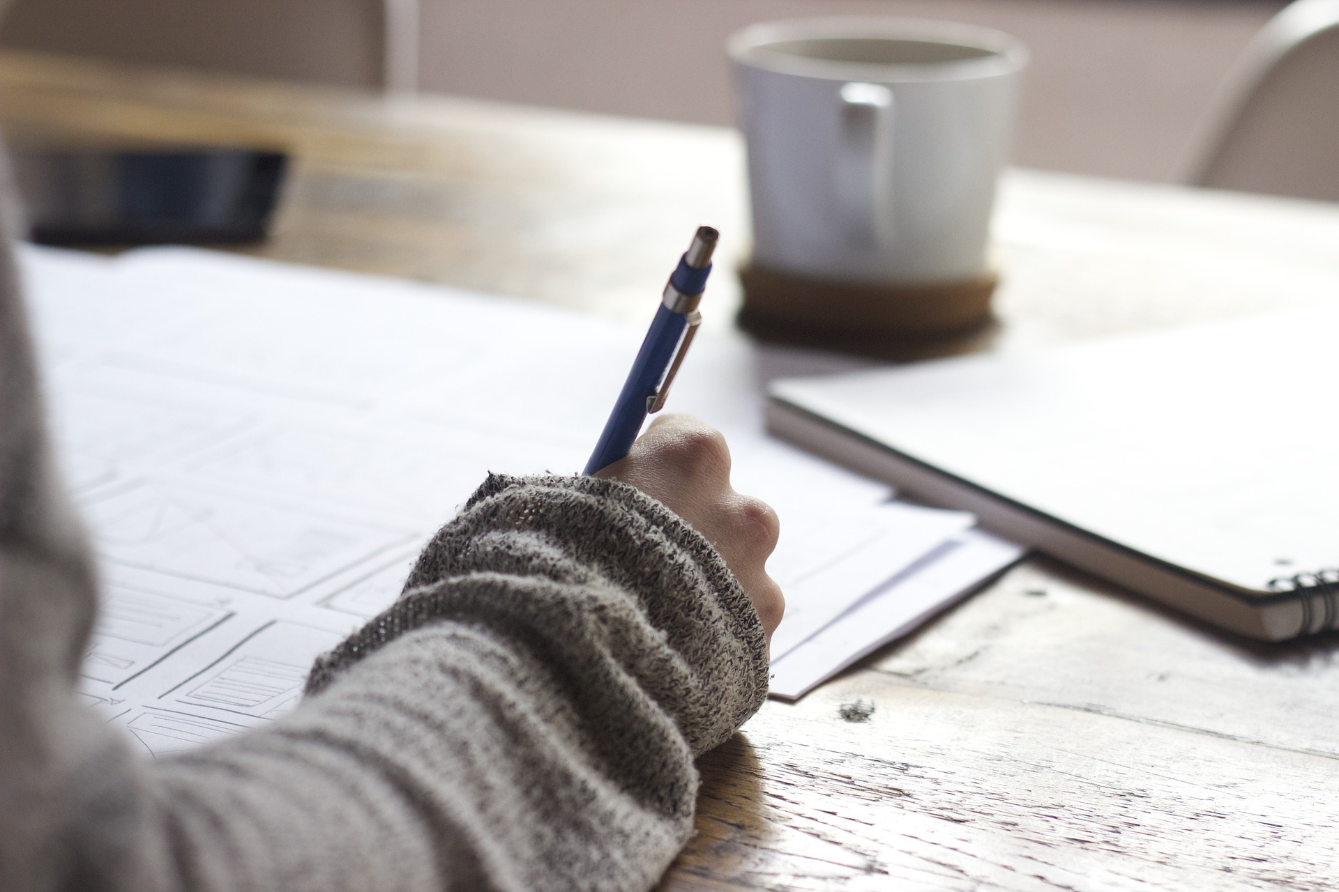 Schreibtisch mit Hand, die einen Stift hält (Foto: Pixabay, CC0)